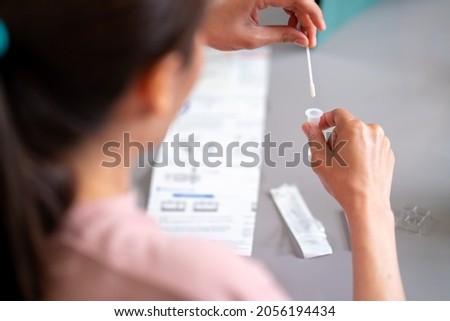 Asian woman using rapid antigen test kit for self test COVID-19 epidemic at home. Adult female place the fabric tip of the swab in the extraction tube and rolling. COVID-19 pandemic protection concept Royalty-Free Stock Photo #2056194434