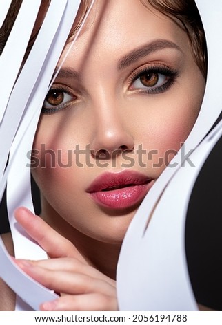 Art portrait of beautiful young woman with brown makeup. Beautiful brunette looks through trafaret paper. Model looking out through  slots white paper.