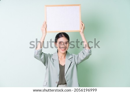 Young Asian businesswoman holding white board on green background