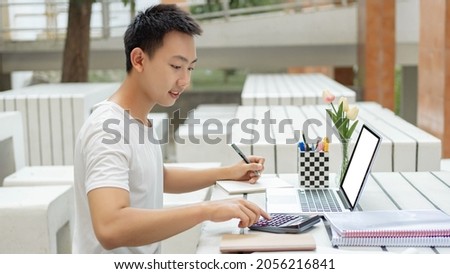 Online studying concept a male student in white t-shirt studying online by using his new white laptop and the calculator in the accounting class. Royalty-Free Stock Photo #2056216841