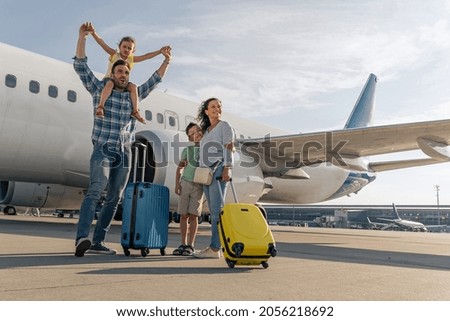 Man, woman and kids standing with suitcases with a big plane in the background