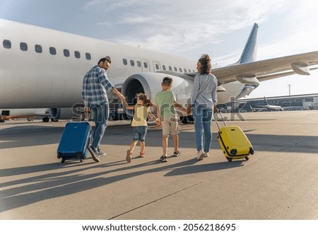 Smiling parents and kids walking with travel bags with a big plane in the background. Trip concept Royalty-Free Stock Photo #2056218695