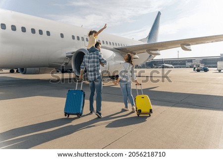 Back view of happy family standing near a large plane with two suitcases outdoor. Trip concept Royalty-Free Stock Photo #2056218710