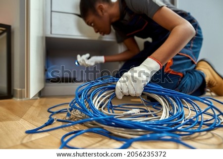 Closeup blue and white cables in female hand. African woman on floor holding cables and lighting on router in cabinet. Network service worker. Selective focus. Royalty-Free Stock Photo #2056235372