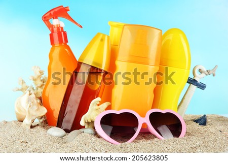 Bottles with suntan cream and sunglasses, on blue background