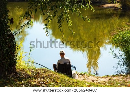 Angler fishing at forest lake in october sunny day. Golden autumnal landscape with  blue sky reflected in calm water. Autumn in Ile-de-France, France.  Active holidays in nature, healthy lifestyle. Royalty-Free Stock Photo #2056248407