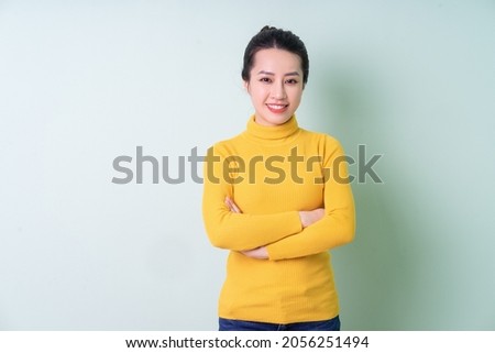 Beautiful young Asian woman wearing sweater on green background Royalty-Free Stock Photo #2056251494