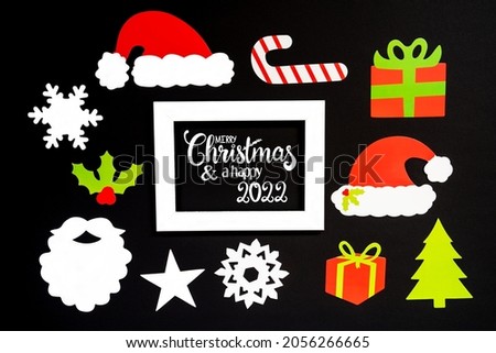 Frame With English Text Merry Christmas And A Happy 2022. Paper Christmas Decoration Like Santa Hat, Gift, Snowflake, Star. Black Background