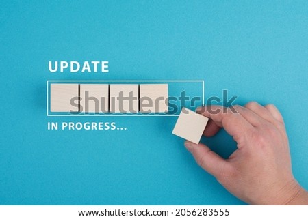 The words update in progress are standing beside the loading bar, hand puts last cube to the upload, blue colored background Royalty-Free Stock Photo #2056283555