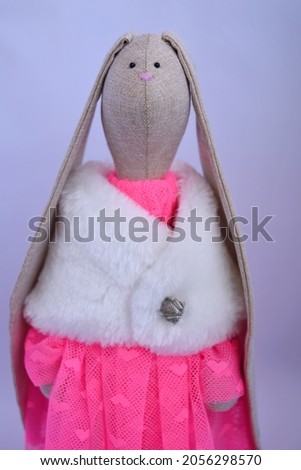 Cute Handmade textile bunny toy in beautiful pink coloured tulle dress and white artificial fur coat.
The background is white