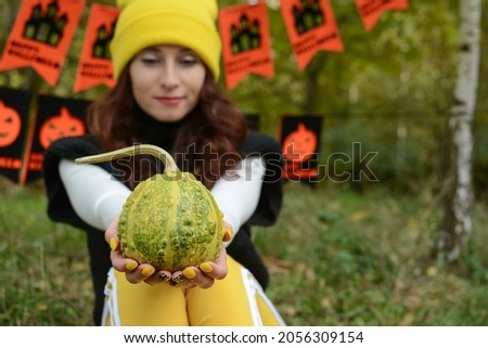 Halloween. A pumpkin in the hands of a girl against the background of a festive Halloween decor in the form of black and orange flags with symbols. The girl is holding a pumpkin.