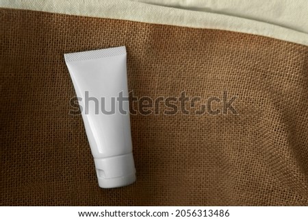 Mockup facial organic skincare white tube bottle product with blank label on hessian or burlap cloth texture background with copy or negative space