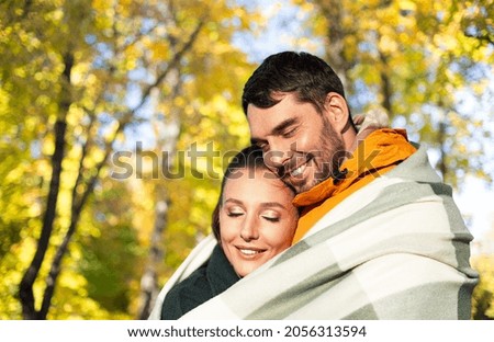 love, season and people concept - happy smiling couple in warm blanket over autumn park background