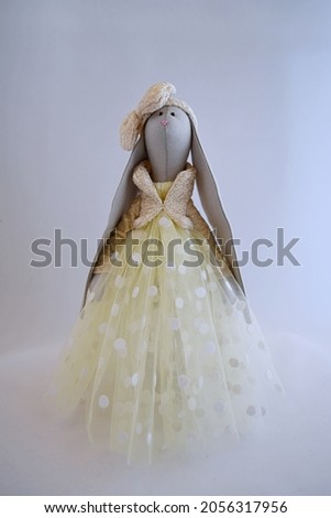 Cute Handmade textile bunny toy in beautiful tulle dress with beige dots and shiny golden jacket. Decorated with a handmade bow.
The background is white. 