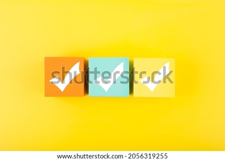 Three checkmarks on multicolored toy cubes on bright yellow background. Concept of questionary, kids related checklist, to do list, planning, business or verification. 