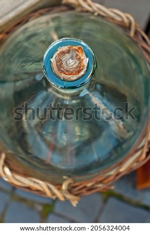 The vine is braided around a large bottle. Wine fermentation basket close up. Glass bottle in a basket.