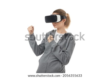 Female in VR goggles standing in fighting pose while experiencing virtual reality and playing video game on white background