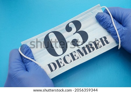 3 december day of month. Doctor holding an antivirus mask in blue medical gloves on a blue background. Protection from disease