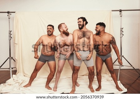 Being natural is fun. Four body positive young men laughing cheerfully while standing together in underwear. Self-confident young men embracing their natural bodies in a studio.