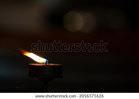 Closeup Candle and its bright light growing in the dark background with bokeh and available copy space. Spiritual, prayer and religious concept. Royalty-Free Stock Photo #2056371626