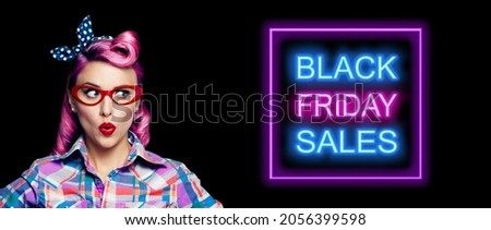 Black Friday Sales, discounts, rebates, trade deals concept - excited surprised pin up woman in red glasses looking sideways. Purple hair girl in pinup rockabilly style. Neon light sign. Wide image.