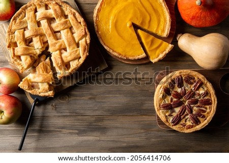 Three homemade autumn pies on wooden background. Traditional American desserts. Pies with pumpkin, apple and pecan for Thanksgiving day. Top view, copy space. 