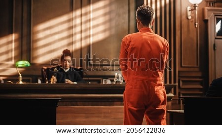 Court of Law and Justice Trial Proceedings: Law Offender in Orange Jumpsuit is Questioned and Giving Testimony to Judge, Jury. Criminal Denying Charges, Pleading, Inmate Denied Parole. Royalty-Free Stock Photo #2056422836