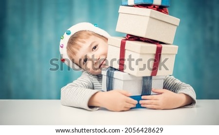 Cute child sitting at the table with stack of giftboxes. Concept of Christmas and New Year celebrating.