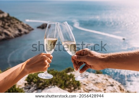 Hands holding champagne glasses over the sea. Romantic vacation. Two hands holding champagne glasses on the background of the sea. A couple in love drinks champagne on the seashore. Copy space Royalty-Free Stock Photo #2056428944