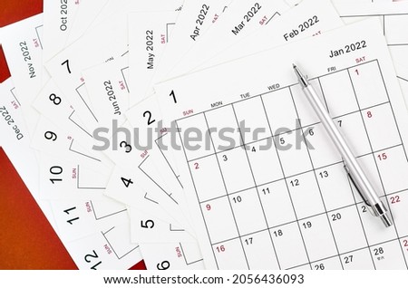 Many blank monthly 2022 calendar sheet with pen on red background.