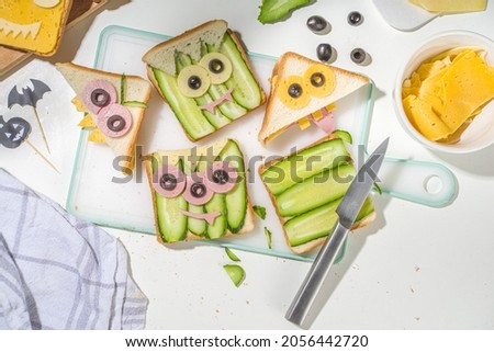 Various funny monster Halloween sandwiches. Cooking creative breakfast snack toasts with cheese, Halloween kids party food, mother woman hands in picture top view