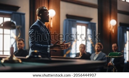 Court of Justice and Law Trial: Male Public Defender Presenting Case, Making Passionate Speech to Judge, Jury. African American Attorney Lawyer Protecting Client's Innocents with Supporting Argument. Royalty-Free Stock Photo #2056444907