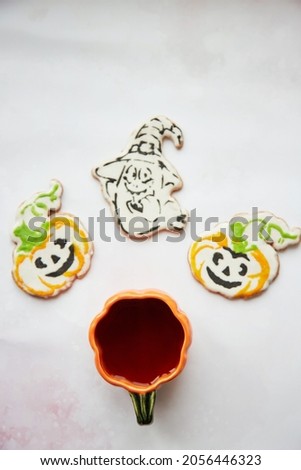 Halloween creative concept: pumpkin cup and homemade cookies in shape of cute pumpkins and ghost closeup. Aesthetic autumn mood or trick or treat concept. Autumn cozy home concept