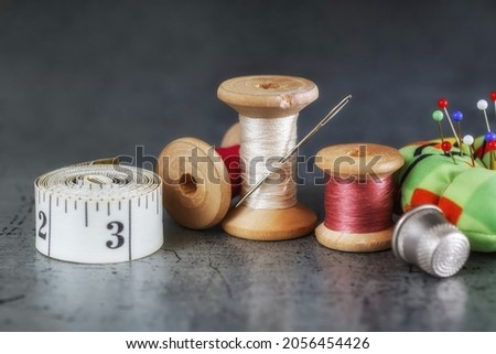 Multicolored threads on a wooden spool, sewing needle with scissors thimble and tailor's tape on an old surface. Sewing thread background. Retro style. Selective focus