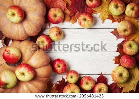 Autumn background with pumpkins, ripe apples and fallen maple leaves on the white wooden boards with a copy space