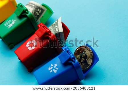 The concept of the collapse of the dollar and bitcoin. Trash cans of different colors with discarded money and bitcoins on a turquoise background. Bitcoin is in the trash. Side view.
