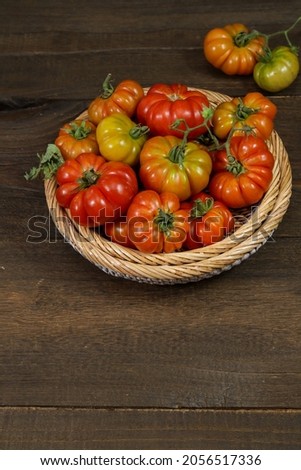 Fresh colorful ripe Fall heirloom tomatoes in rattan basket over wooden background, top view, copy space.