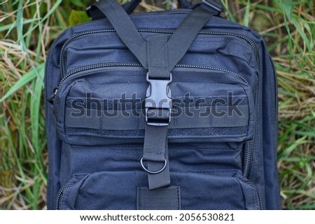 part of a black tactical backpack with harnesses with a plastic latch and a metal ring on the street against a background of green grass