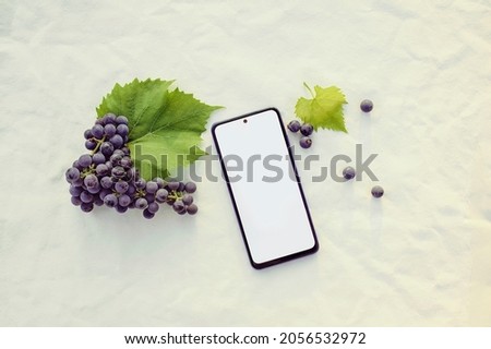 Mockup of an electronic device of a modern smartphone with a bunch of grapes on a beige background. Sunset. Top view