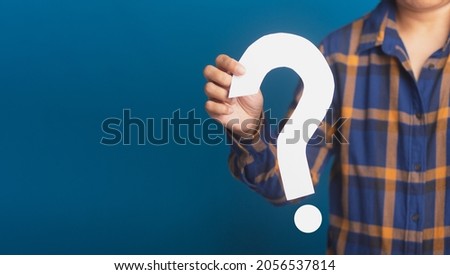 Hand of a businessman holding a white question mark paper while standing with a blue background. Close-up photo. Space for text