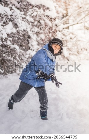 The child plays snowballs against the background of a snow forest.