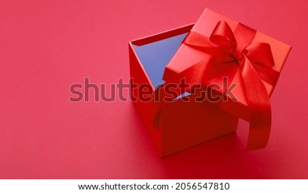 Christmas gift box with ribbon bow open on red color background, Valentine surprise, New Year holiday present, satin curly decoration. Copy space, greeting card template