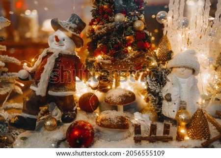 Funny winter toy snowman and snow covered Christmas tree with golden lights on a festive storefront. New Year and Merry Christmas decorations and a magical winter atmosphere.