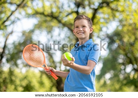 Confident friendly boy with racket and tennis ball Royalty-Free Stock Photo #2056592105
