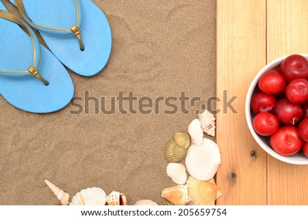 Slippers and plums on wood and sand