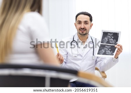 Photo of doctor wearing lab coat showing an ultrasound result to his patient.