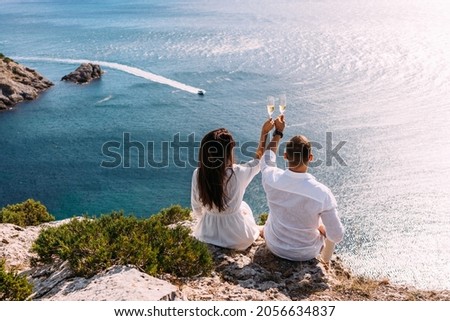 A couple in love drinking champagne on the seashore, rear view. The newlyweds are celebrating their engagement. A man and a woman sitting with their backs to the camera drinking champagne by the sea Royalty-Free Stock Photo #2056634837