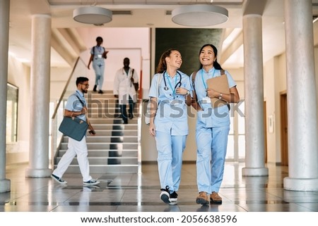 Happy nursing student and her Asian friend walking through a corridor at medical university.