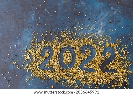 Numbers 2022 on a blue background strewn with gold confetti. Greeting Happy New Year, Merry Christmas. Minimalism. There are no people in the photo. There is an empty space for an inscription.