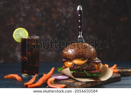 Hot burger with a glass of ice drink on a wooden background. Rustic style